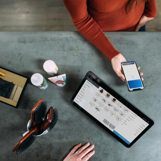 Overhead shot of two people sitting across a table from one another, with one navigating through a smartphone and the other looking at a tablet