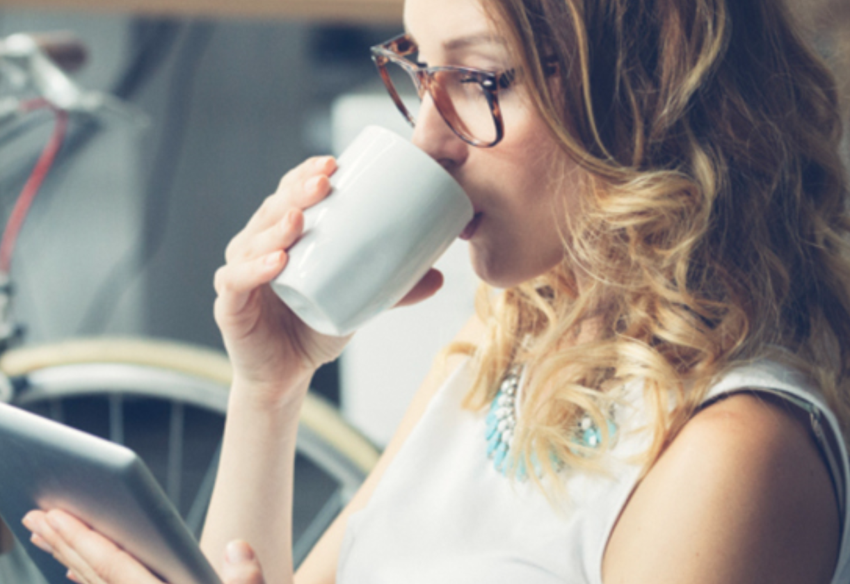 A woman drinking a beverage and looking at a tablet